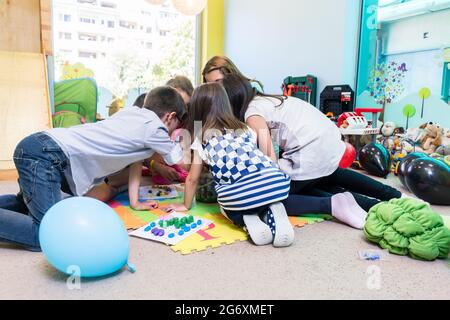 Gruppo di bambini prescolastica che circondano il loro insegnante esperto durante un'attività educativa in classe di un moderno asilo Foto Stock