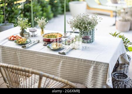 Il tavolo in giardino è coperto da una tovaglia e decorato con fiori e candele con cibo per due persone. Cena estiva all'aperto. Foto Stock