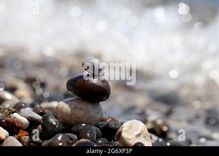 Torre di ciottoli su sfondo sfocato delle onde del mare. Vacanza estiva, concetto di equilibrio e relax Foto Stock