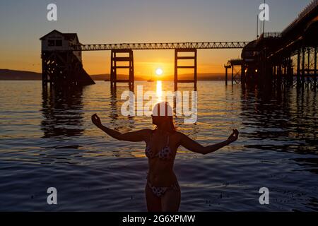 Nella foto: Natasha Jenkins in mare durante l'alba, visto attraverso la stazione delle barche RNLI a Mumbles, vicino a Swansea, Galles, Regno Unito. Domenica 13 Giugno 2021 Re: Foto Stock