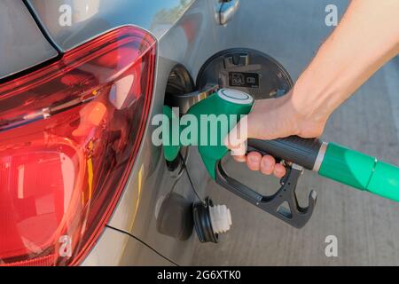 Le mani dell'uomo tengono la pompa di benzina, rifornendo la sua auto con carburante vicino attraverso le strade della città. Industria energetica. Stazione di benzina business / mercato Foto Stock