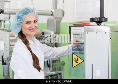 Primo piano della mano di un ingegnere di produzione femminile che regola le impostazioni di una macchina industriale durante il lavoro in una moderna fabbrica di cosmetici Foto Stock