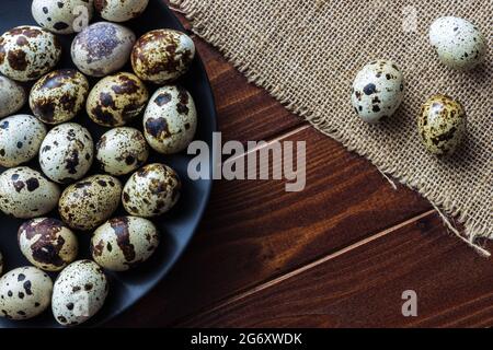 Uova di Quail in ciotola di legno e su piatto scuro su legno; uova piccole macchiate; delicatezza; concetto rustico naturale Foto Stock