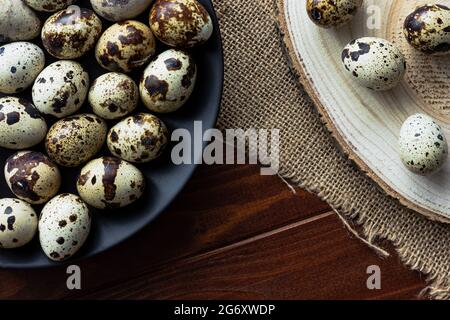 Uova di Quail in ciotola di legno e su piatto scuro su legno; uova piccole macchiate; delicatezza; concetto rustico naturale Foto Stock