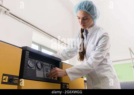 Vista laterale di un ingegnere femminile che scrive osservazioni per un rapporto sulle attrezzature e la produzione, mentre si trova vicino a una macchina di compressore in un moderno Foto Stock