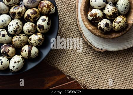 Uova di Quail in ciotola di legno e su piatto scuro su legno; uova piccole macchiate; delicatezza; concetto rustico naturale Foto Stock