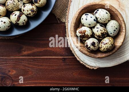 Uova di Quail in ciotola di legno e su piatto scuro su legno; uova piccole macchiate; delicatezza; concetto rustico naturale Foto Stock