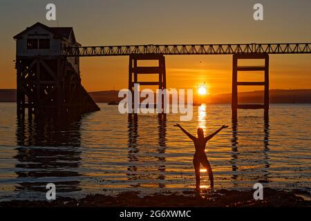 Nella foto: Natasha Jenkins in mare durante l'alba, visto attraverso la stazione delle barche RNLI a Mumbles, vicino a Swansea, Galles, Regno Unito. Domenica 13 Giugno 2021 Re: Foto Stock