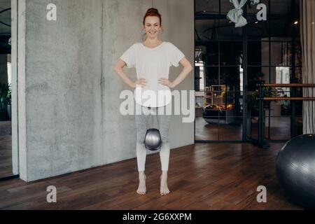 Donna sportiva rossa che tiene la palla mini pilates con le ginocchia Foto Stock
