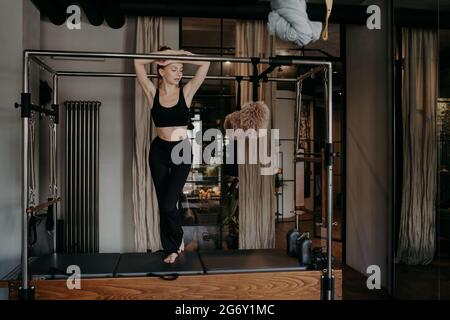 Giovane femmina caucasica sottile che riposa su bar di pilates riformatore cadillac Foto Stock