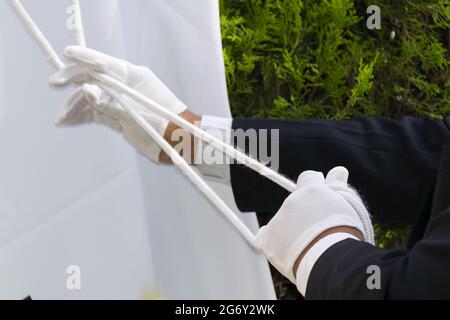 Mani dell'uomo con guanti che alzano bandiera in America Latina, dettaglio con luce naturale. Foto Stock