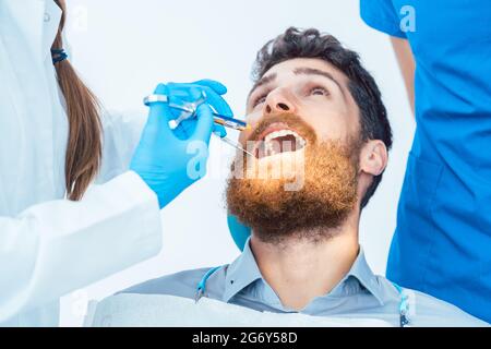 Vista ravvicinata ad angolo basso di un uomo con la bocca aperta durante una procedura medica presso l'ufficio odontoiatrico di una dentista femminile esperta Foto Stock