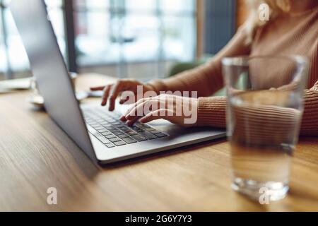 Primo piano di una donna che lavora su un computer portatile wireless al bar Foto Stock
