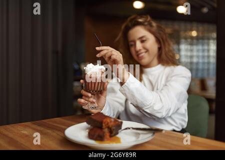Donna sorridente che mangia gustoso dessert e beve cacao Foto Stock