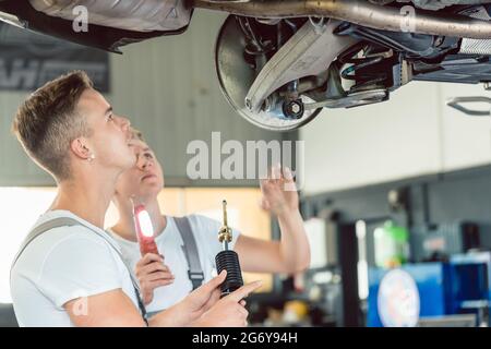 Vista laterale di un tecnico meccanico automatico sostituzione degli ammortizzatori di un auto sollevata, mentre si lavora insieme con il suo collega in una moderna automobile r Foto Stock