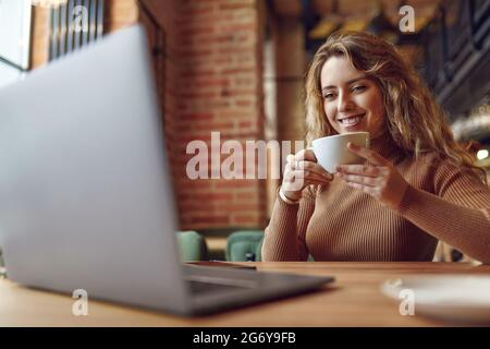 Donna che ama la bevanda calda mentre lavora su un computer portatile Foto Stock