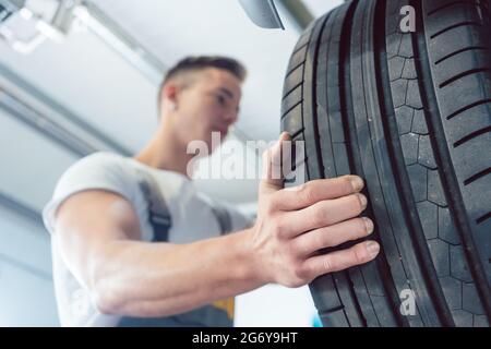 Vista ad angolo basso della mano di un meccanico specializzato che tiene un nuovo pneumatico di alta qualità durante il lavoro in un moderno negozio di riparazione di automobili Foto Stock