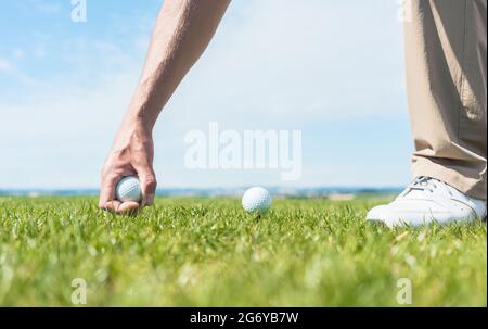 Primo piano della mano di un giocatore maschile professionista, prendendo una palla dall'erba verde di un campo da golf durante una partita individuale in una giornata di sole sume Foto Stock