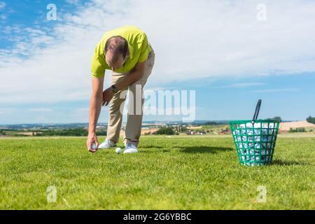 Primo piano della mano di un giocatore maschile professionista che prende una palla dall'erba verde di un campo da golf, durante una partita individuale in una giornata di sole sume Foto Stock