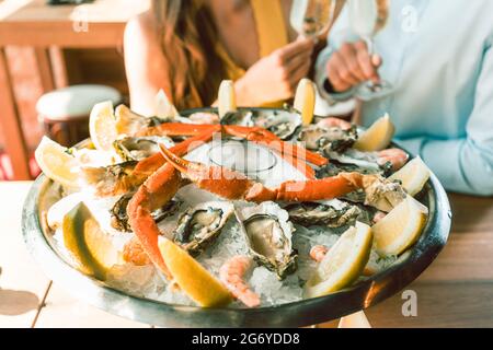 Primo piano di ostriche fresche e granchi serviti su ghiaccio con fette di limone alla tavola di un giovane romantico coppia che mangia al ristorante Foto Stock