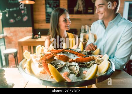 Primo piano di ostriche fresche e granchi serviti su ghiaccio con fette di limone alla tavola di un giovane romantico coppia che mangia al ristorante Foto Stock