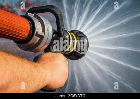 Closeup di una mano di un pompiere che tiene una lancia e spruzzi d'acqua pressurizzata sul fuoco Foto Stock
