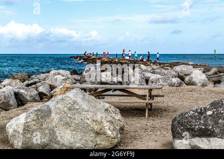 Venice Florida South Jetty con persone che pescano sul molo e un tavolo da picnic vuoto e grandi massi del molo in primo piano. Foto Stock