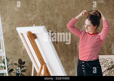 Donna che dispone i capelli mentre si trova davanti al cavalletto Foto Stock