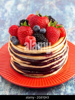 Stack di frittelle di Berry con Compote sparso su un rustico tavolo di legno blu Foto Stock