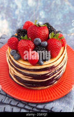 Stack di frittelle di Berry con Compote sparso su un rustico tavolo di legno blu Foto Stock