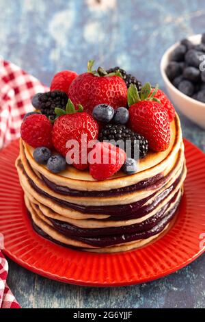 Stack di frittelle di Berry con Compote sparso su un rustico tavolo di legno blu Foto Stock