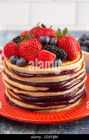 Stack di frittelle di Berry con Compote sparso su un rustico tavolo di legno blu Foto Stock