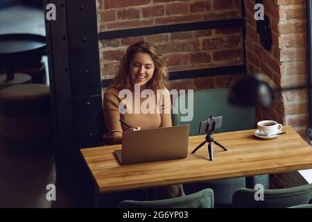 Donna sorridente seduta al tavolo con computer portatile e smartphone Foto Stock