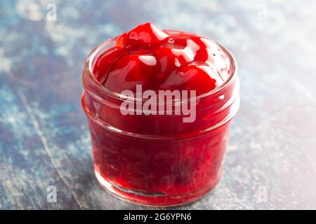 Un vaso di inscatolamento di vetro riempito con il ripieno di torta di ciliegia su un tavolo di legno Foto Stock