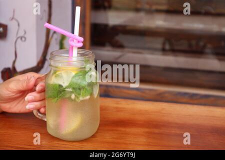 Closeup un bicchiere di appetitosa limonata ghiacciata in mano di Donna con fuoco selettivo Foto Stock