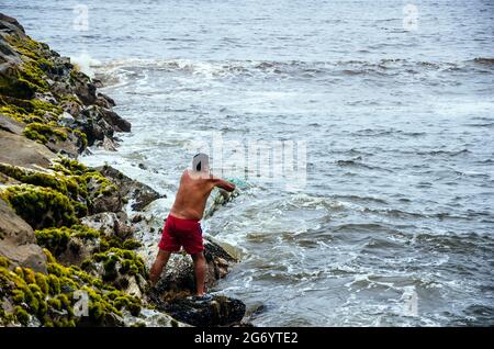 Pescatore che tira la rete di pesca sulle spiagge di Lima, Perù. Foto Stock