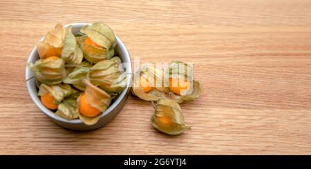 Frutti di Physalis su un tavolo di legno. Bacche di fisalis dolci gialle in una tazza su sfondo di legno. Foto Stock