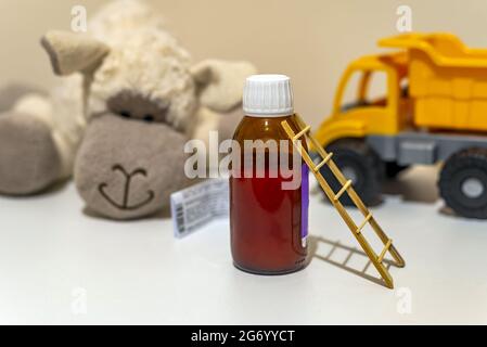 Piccola scala in legno e una piccola bottiglia di sciroppo medico con giocattoli per bambini sullo sfondo Foto Stock