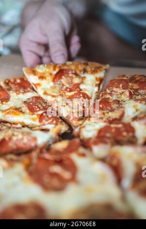 L'uomo corto prende un pezzo di pizza con la mano. Messa a fuoco selettiva, sfocatura, primo piano Foto Stock