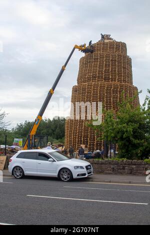 4 luglio 2021 giovani in cima al falò molto alto fatto da migliaia di pallet industriali in legno in preparazione per le celebrazioni del 12 luglio Foto Stock