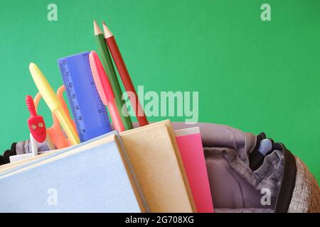 Zaino da scuola, libri, notebook, cancelleria, sfondo verde. Foto Stock