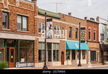 Holland, MI, USA - 8 giugno 2008: Quartiere storico. Fila di piccole facciate di mattoni rossi e marroni di negozi con una coppia di colorati striscioni di strada artistica in Foto Stock