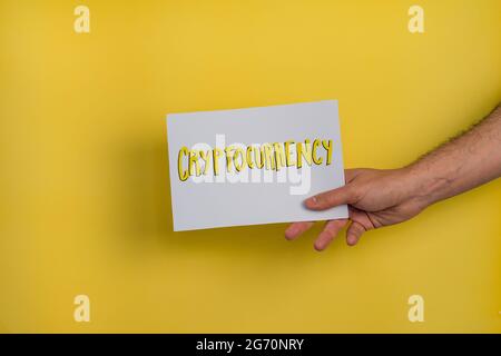 Un primo piano di un uomo che tiene un documento con la parola "CRIPTOVALUTA" su sfondo giallo Foto Stock