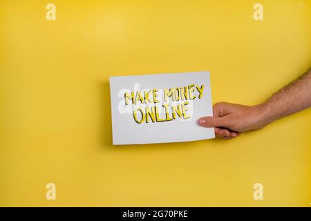 Un primo piano di un uomo che tiene una carta con la parola 'MAKE MONEY ONLINE' su uno sfondo giallo Foto Stock