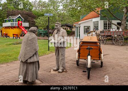 Olanda, MI, USA - 8 giugno 2008: Nelis Dutch Village. Statua dell'uomo che consegna il pane alla signora anziana a Paardelaan in ambiente rurale con edifici, auto Foto Stock