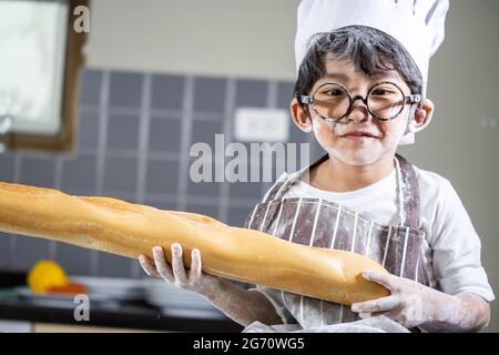 Asian Boy indossare bicchieri cucinare con farina bianca impastare impasto di pane insegna ai bambini pratica cottura ingredienti pane, uova su stoviglie in cucina l Foto Stock