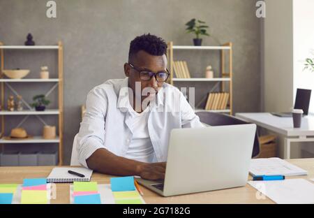 Responsabile esecutivo afro-americano che scrive sul computer portatile seduto alla scrivania dell'ufficio Foto Stock