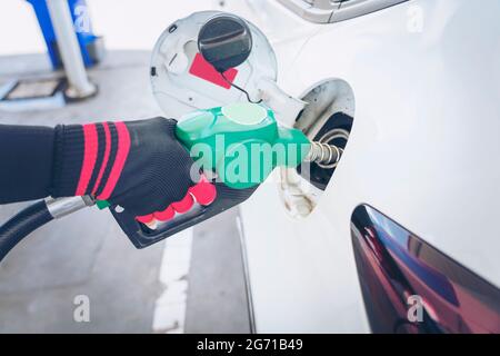 Impianto di rifornimento del veicolo presso il distributore di benzina. Auto bianca al distributore di benzina in fase di rifornimento di carburante. Rifornimento manuale dell'auto con carburante presso la stazione di rifornimento. T Foto Stock