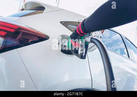 Impianto di rifornimento del veicolo presso il distributore di benzina. Auto bianca al distributore di benzina in fase di rifornimento di carburante. Rifornimento manuale dell'auto con carburante presso la stazione di rifornimento. T Foto Stock