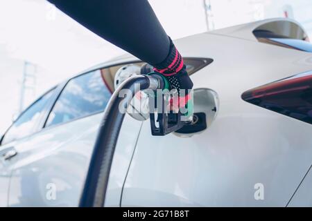 Impianto di rifornimento del veicolo presso il distributore di benzina. Auto bianca al distributore di benzina in fase di rifornimento di carburante. Rifornimento manuale dell'auto con carburante presso la stazione di rifornimento. T Foto Stock